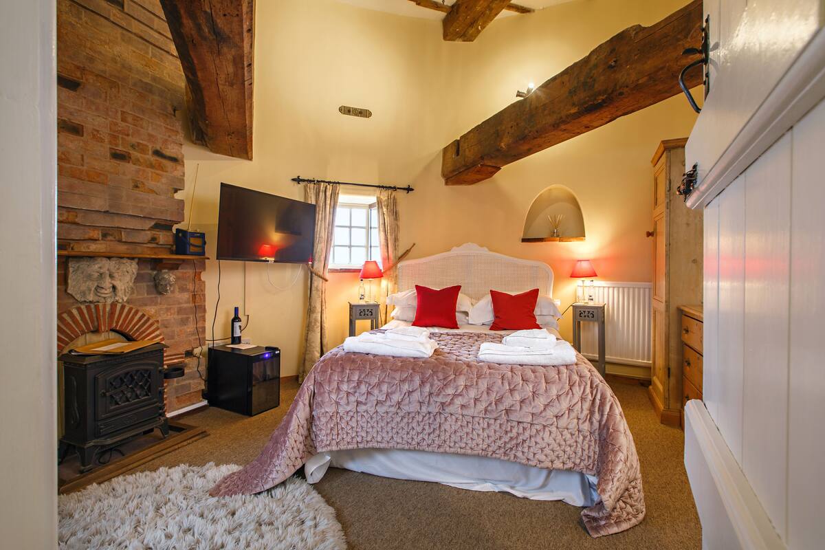 A bedroom with a large bed, a fireplace, and a rustic wooden ceiling.