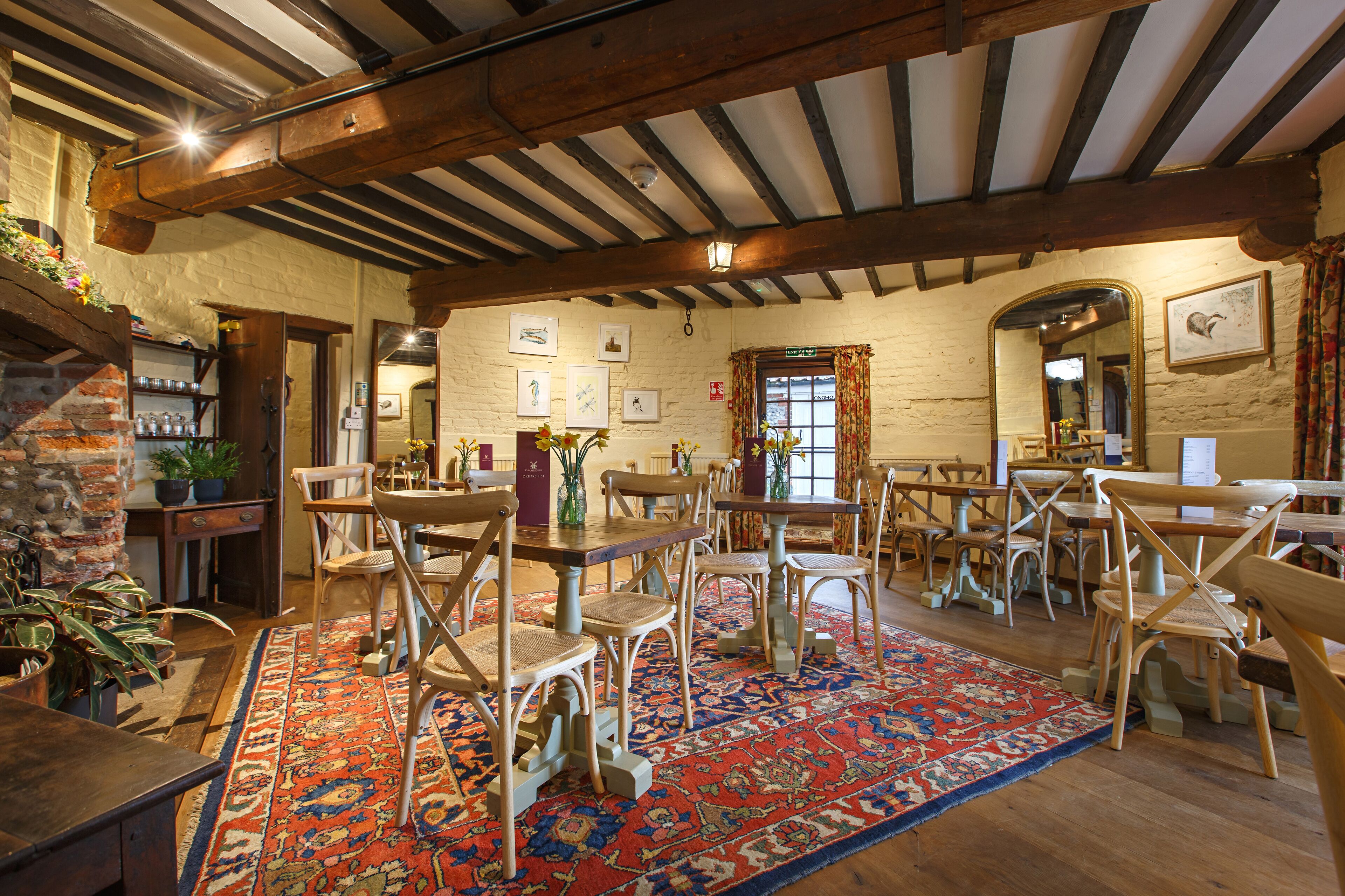 A rustic dining area with wooden tables and chairs, a patterned rug, and a brick wall.