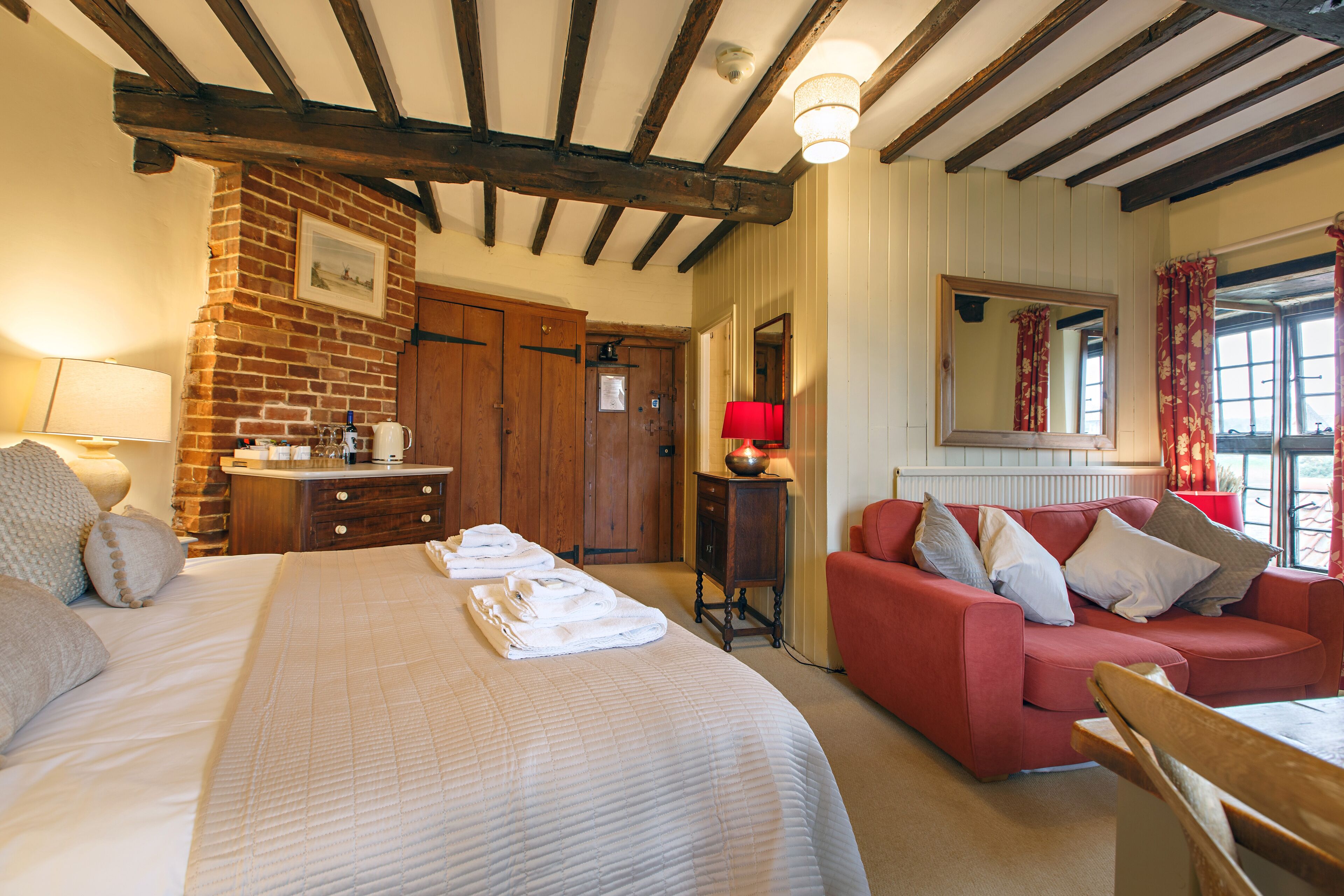 Una habitación de hotel con una cama grande, un sofá rojo, un aparador de madera y una pared de ladrillo.