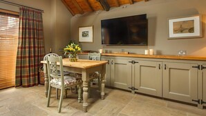 A dining area with a wooden table and chairs, a television mounted above the counter, and a window with blinds. - Cley Windmill (Holt)