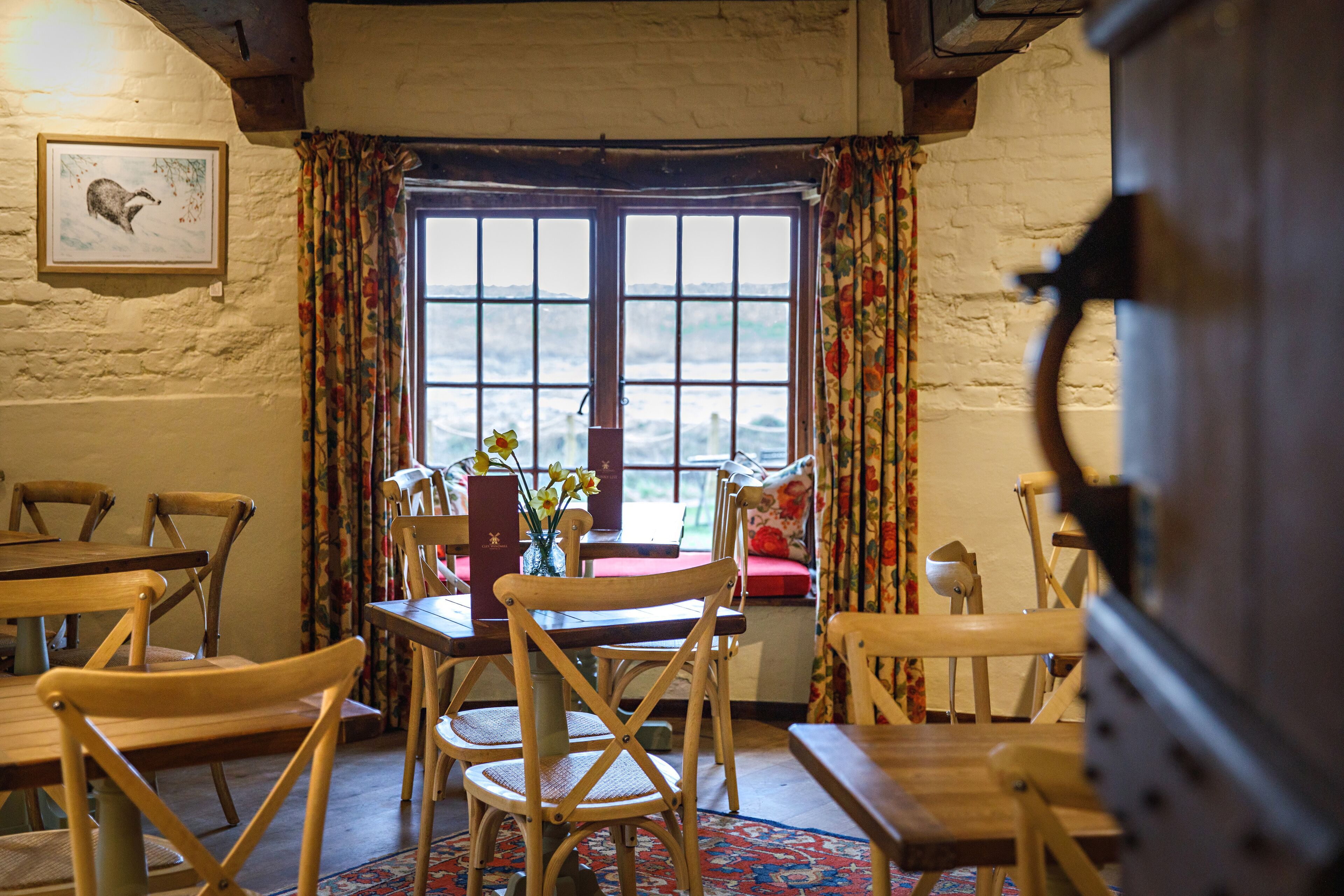 A rustic dining area with wooden furniture, a large window with curtains, and a framed picture on the wall.