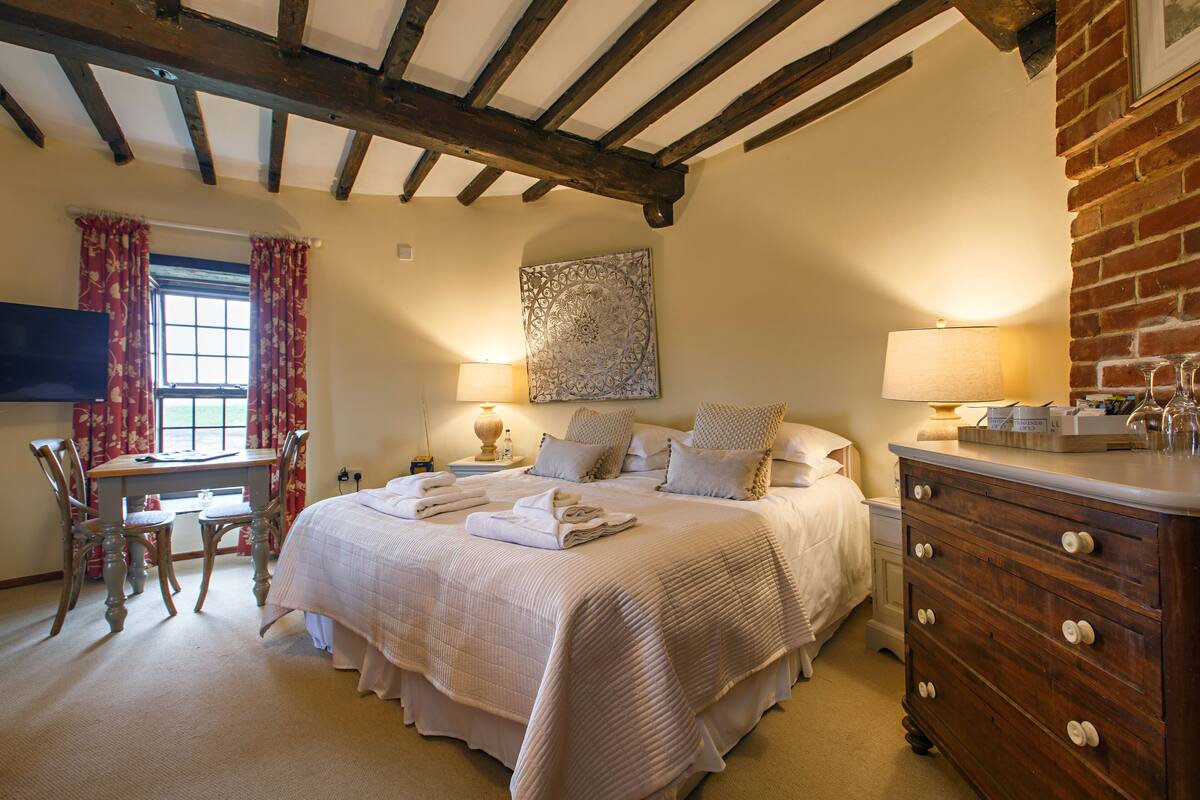 A bedroom with a large bed, wooden headboard, a dresser, a desk, and a window with curtains.