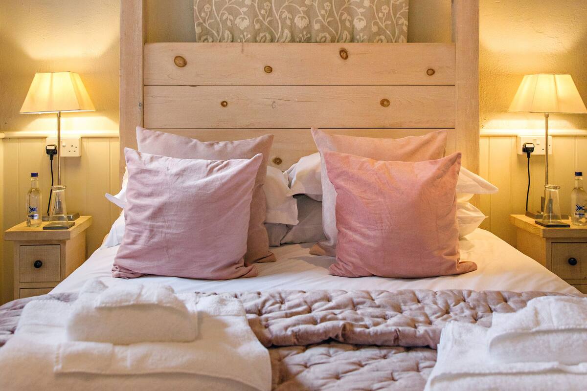 A bedroom with a wooden headboard, two bedside tables with lamps, a bed with pink and white bedding, and a patterned curtain.