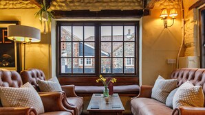 A cozy seating area with leather sofas and a wooden table, a vase with flowers, and a view of buildings through a window. - Cley Windmill (Holt)