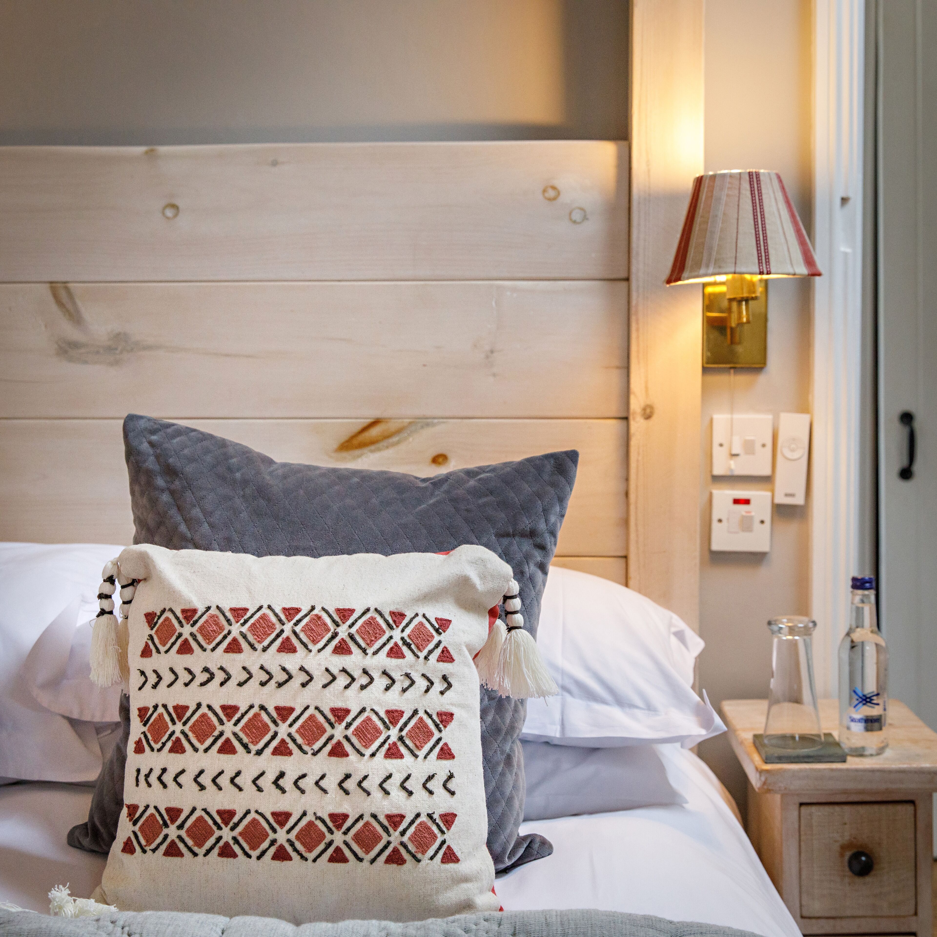 Un lit bien fait, avec un oreiller matelassé, un plaid décoratif et une lampe de chevet.