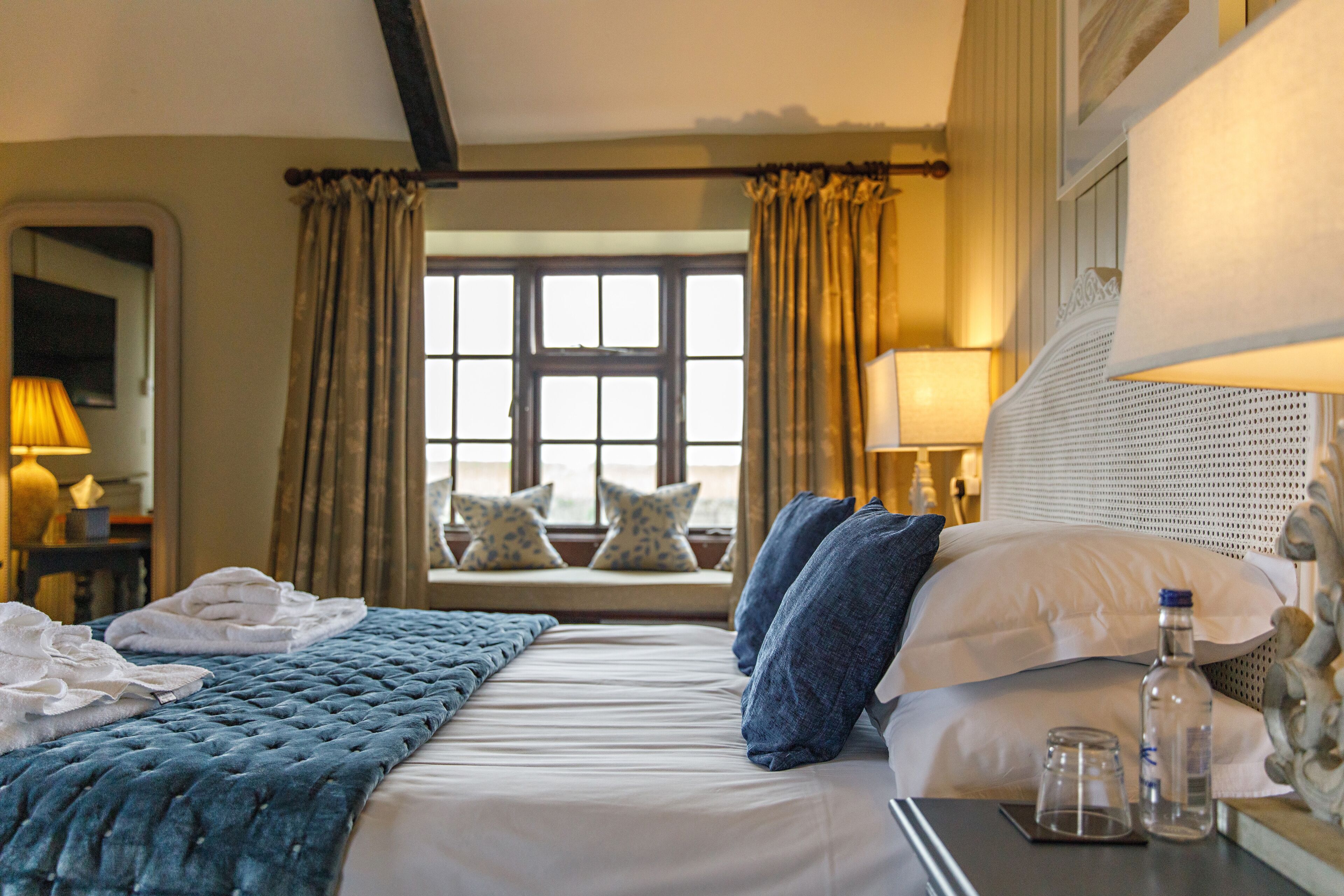 Une chambre d’hôtel avec un lit, une fenêtre avec des rideaux, une table de chevet avec une lampe, et une vue sur l’extérieur.