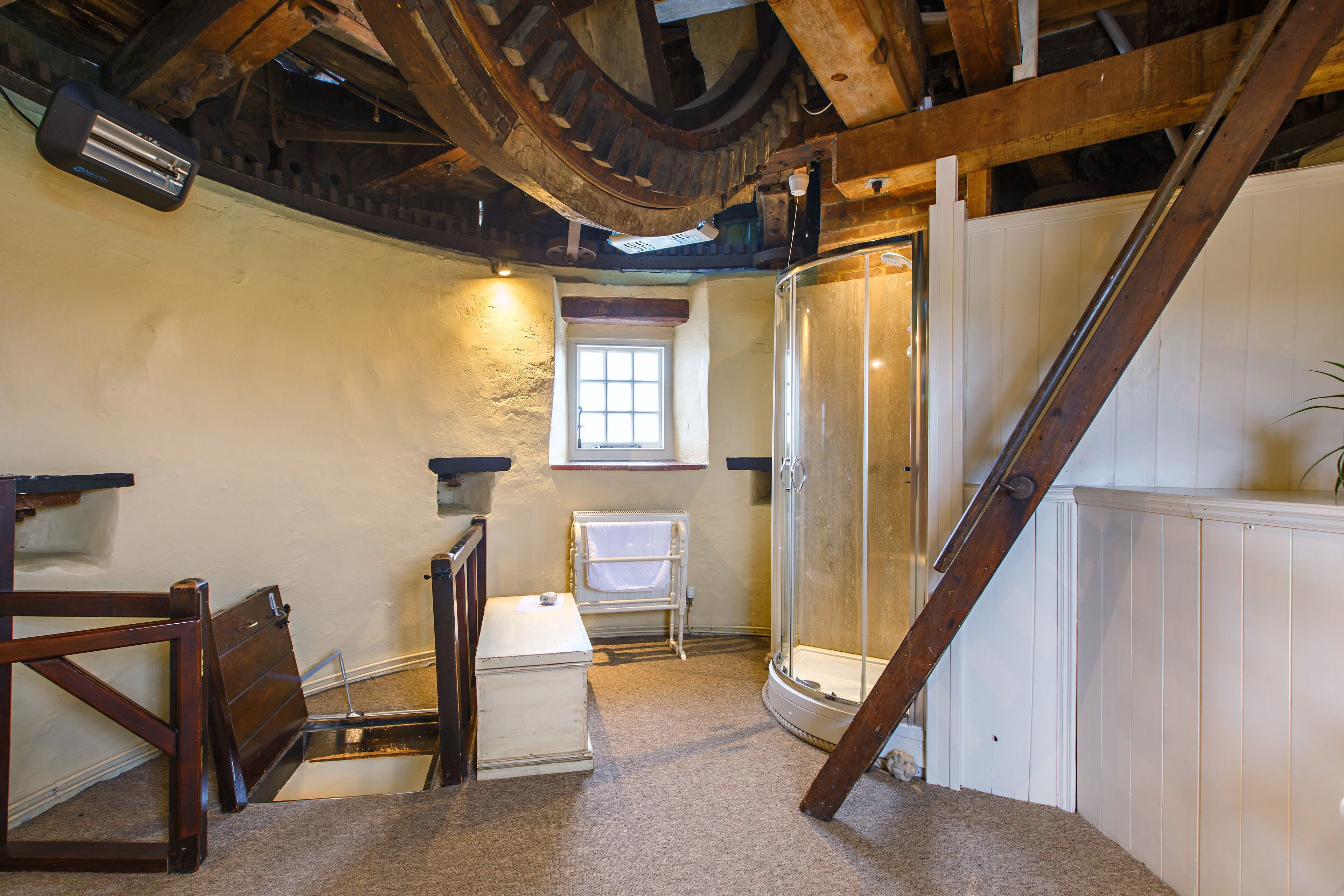 A room with a wooden ceiling, a white radiator, a window, a shower, and a staircase.
