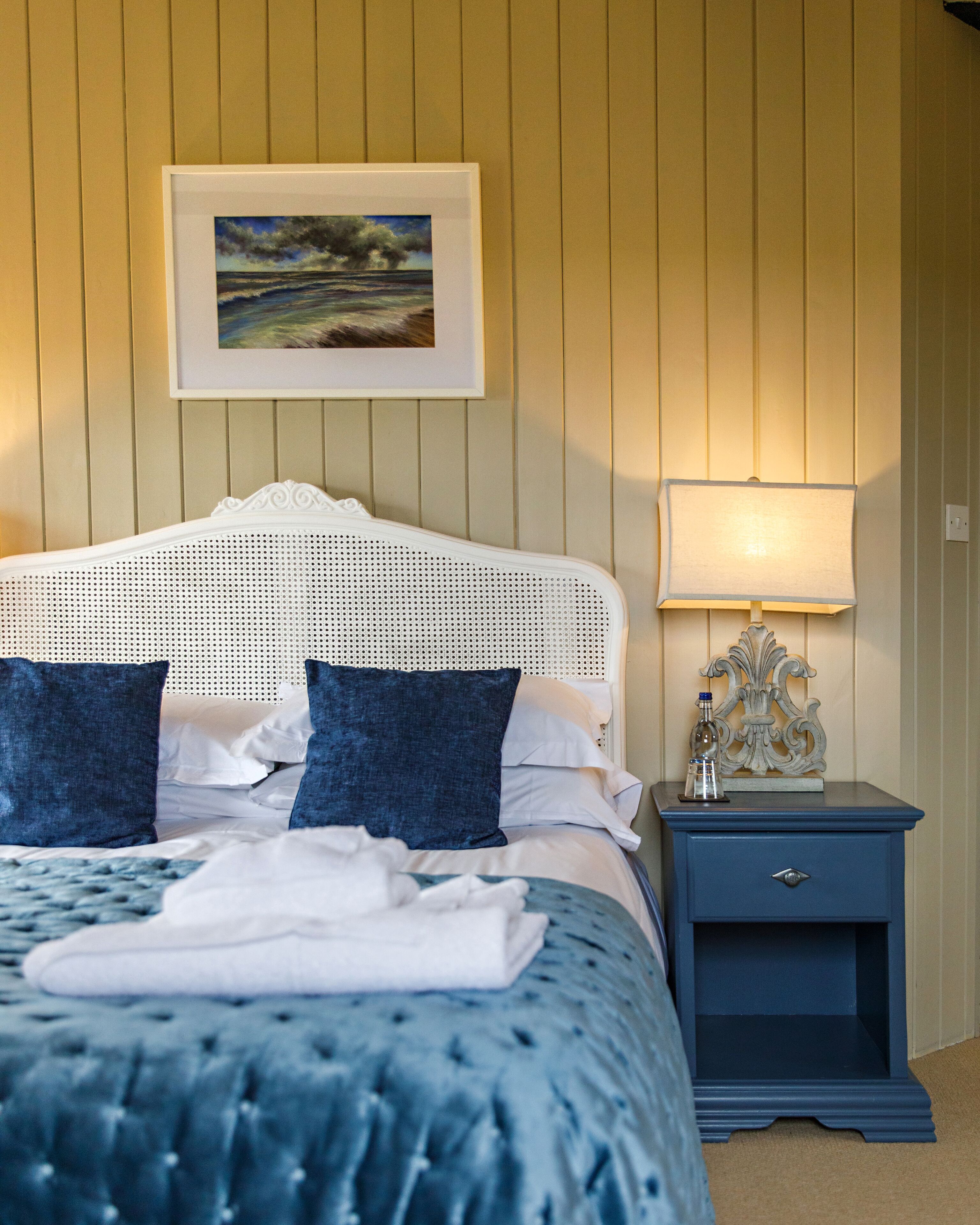Une chambre à coucher avec un lit, des oreillers, une table de chevet, une lampe et un tableau encadré au mur.
