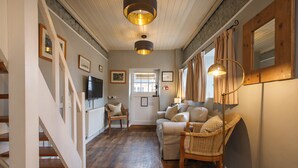 A cozy living room with a sofa, chairs, and a television. A staircase leads to another room. - Cley Windmill (Holt)