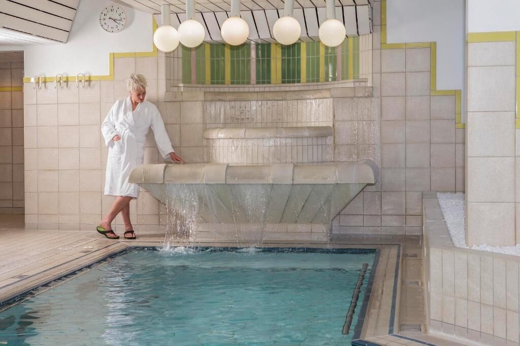 A person in a white robe stepping into a pool with a water feature above.