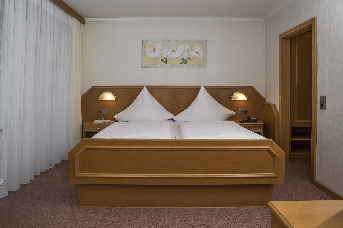 A hotel room with a wooden bed, two bedside lamps, a nightstand, and a painting on the wall.