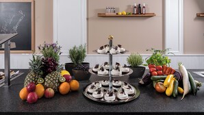 A kitchen counter with a three-tiered dessert stand, fresh fruits, vegetables, and a chalkboard with a greeting. - Kurhotel Unter den Linden (Bad Fuessing)