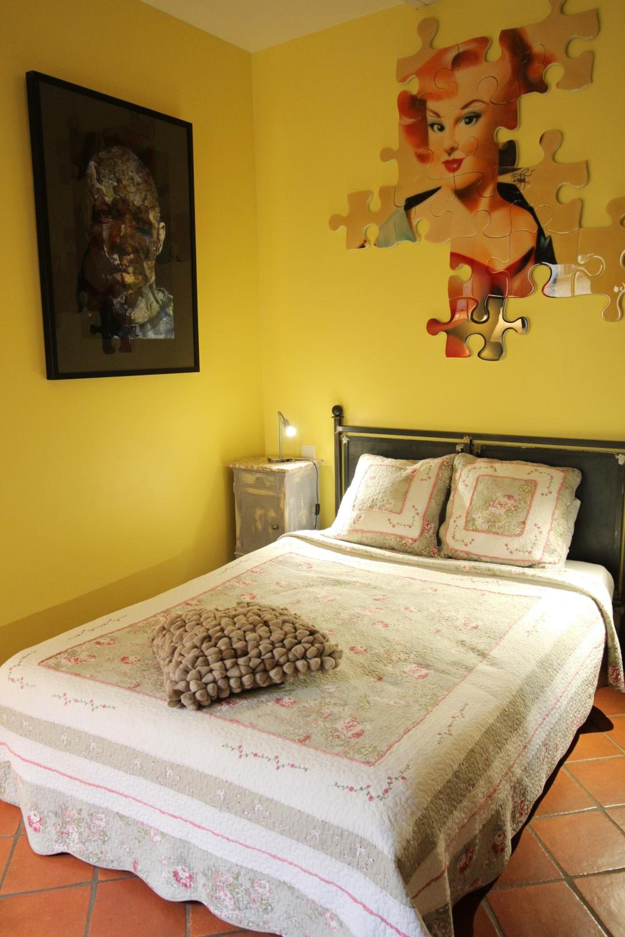 Een slaapkamer met een bed, nachtkastje, lamp en een muur met een ontwerp van puzzelstukjes.