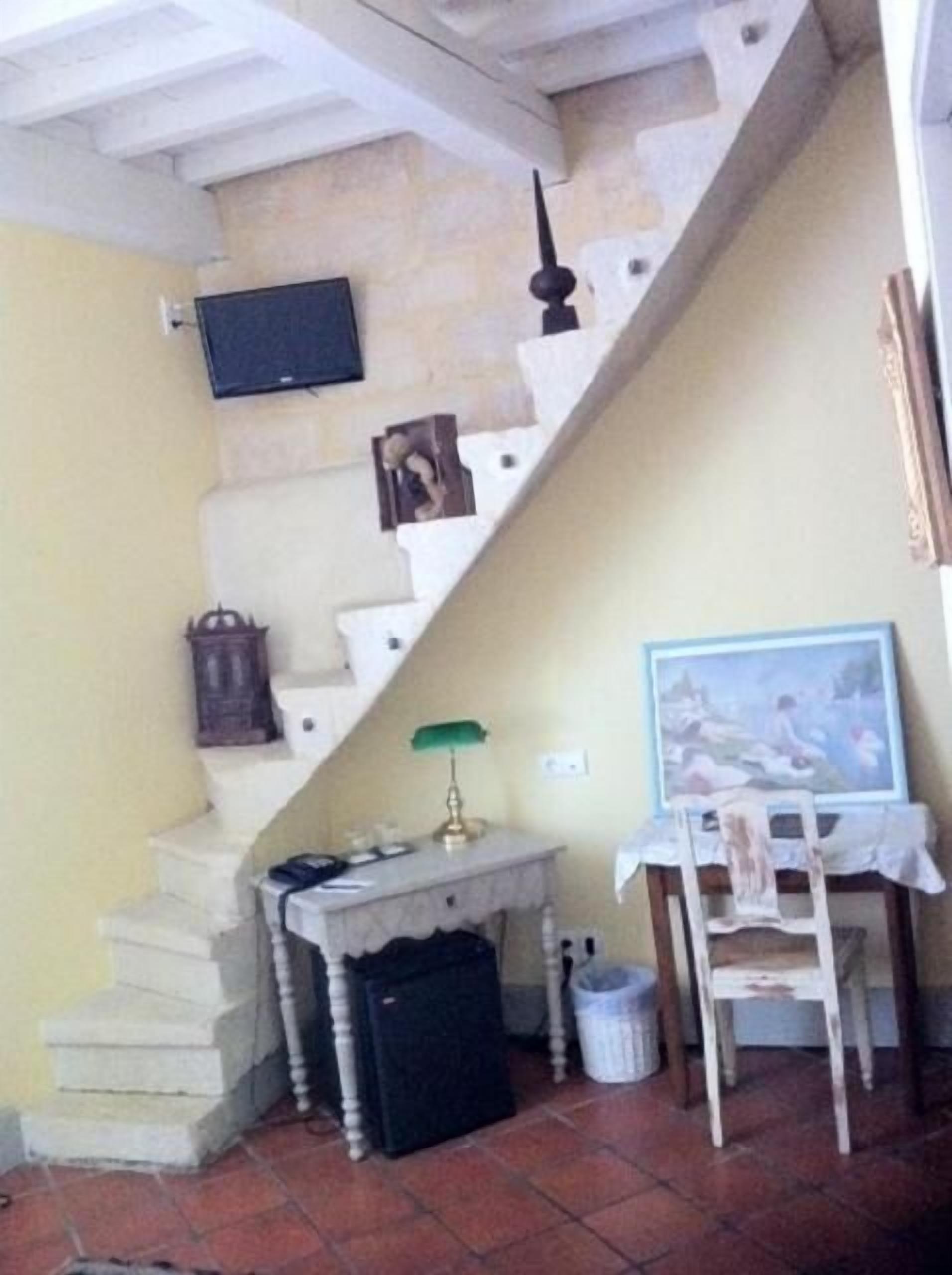 Un escalier menant à un palier où se trouvent un téléviseur, une petite table avec une lampe, une chaise et un tableau accroché au mur.