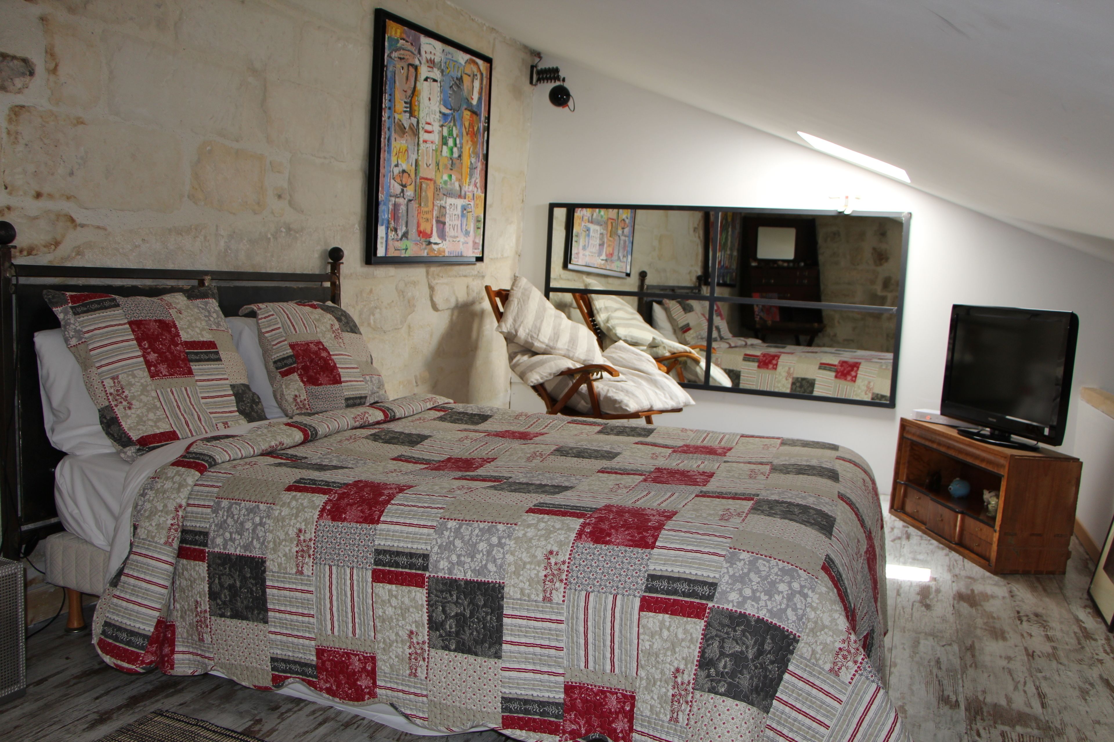 A bedroom with a large bed, a television on a wooden cabinet, and a mirror on the wall.