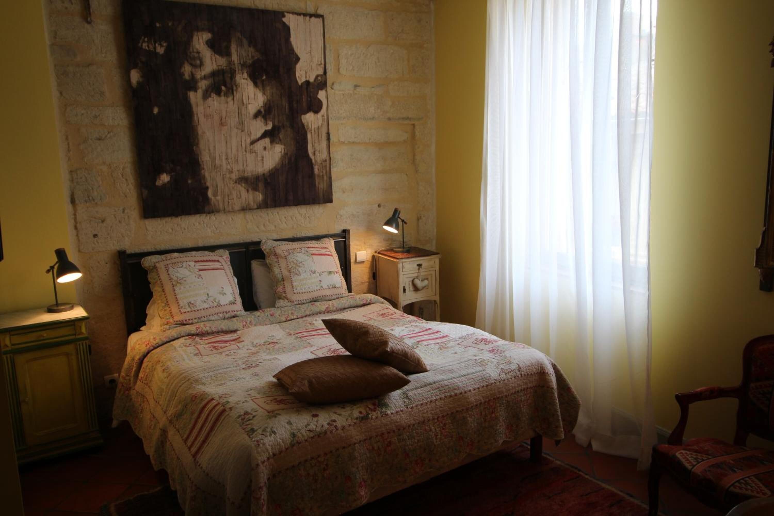 Une chambre à coucher avec un grand lit, une table de chevet, une lampe, une chaise et une œuvre d’art accrochée au mur.