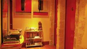 Ein Flur mit einer roten Tür, die mit '6' beschriftet ist, einem Bücherregal mit Büchern und zwei abstrakten Gemälden an der Wand.