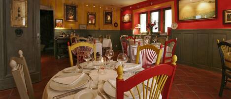 A dining area with tables set for four, chairs, and a bar area in the background.