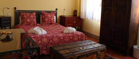 A bedroom with a bed, a wooden chest, a nightstand, a lamp, and a painting on the wall.