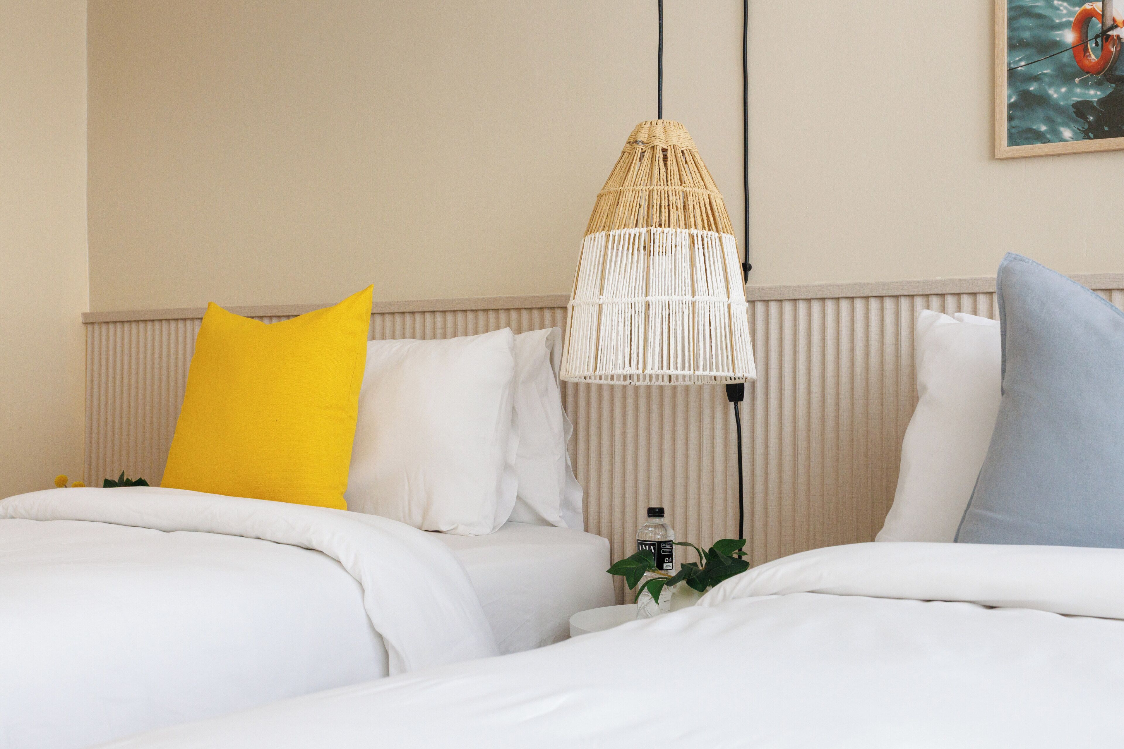 A hotel room with two beds, a hanging light fixture, and a wall-mounted picture.