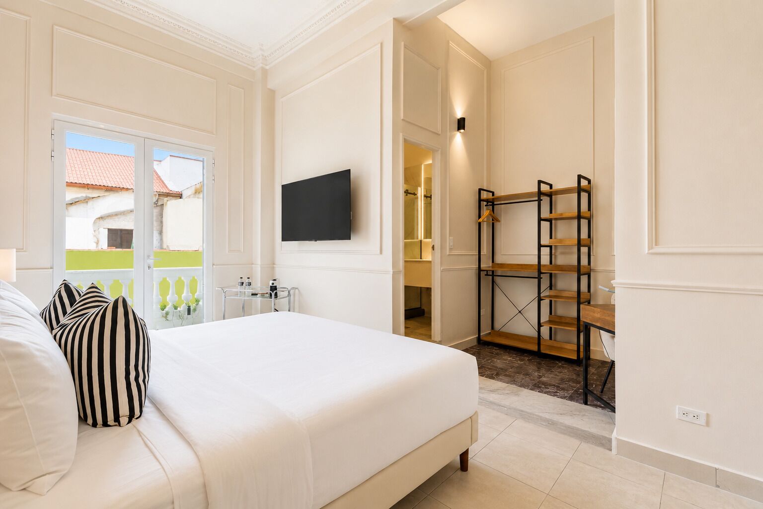 A hotel room with a bed, a TV, a bathroom, and a balcony.