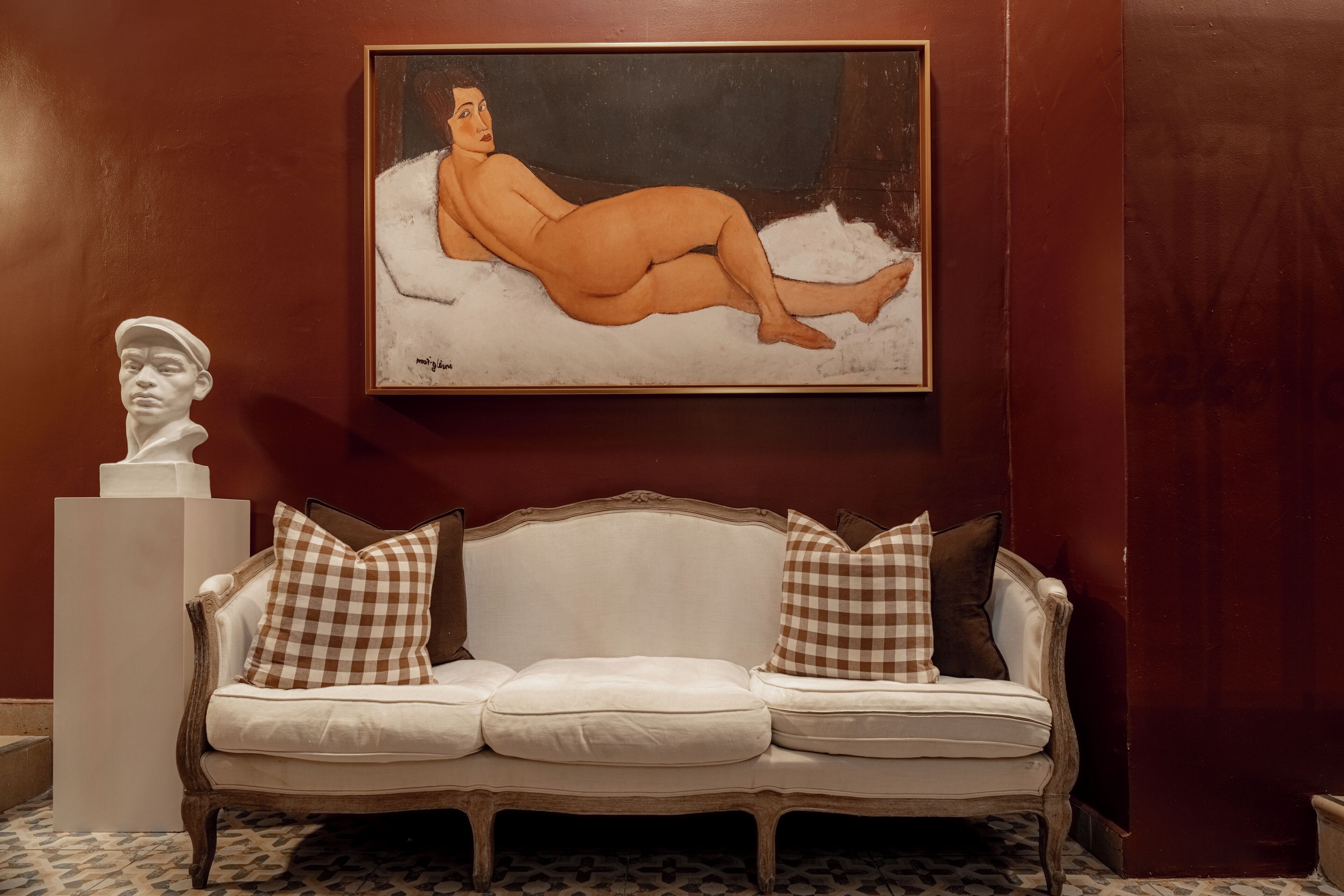 Una habitación con un sofá blanco, un busto y un cuadro en la pared.