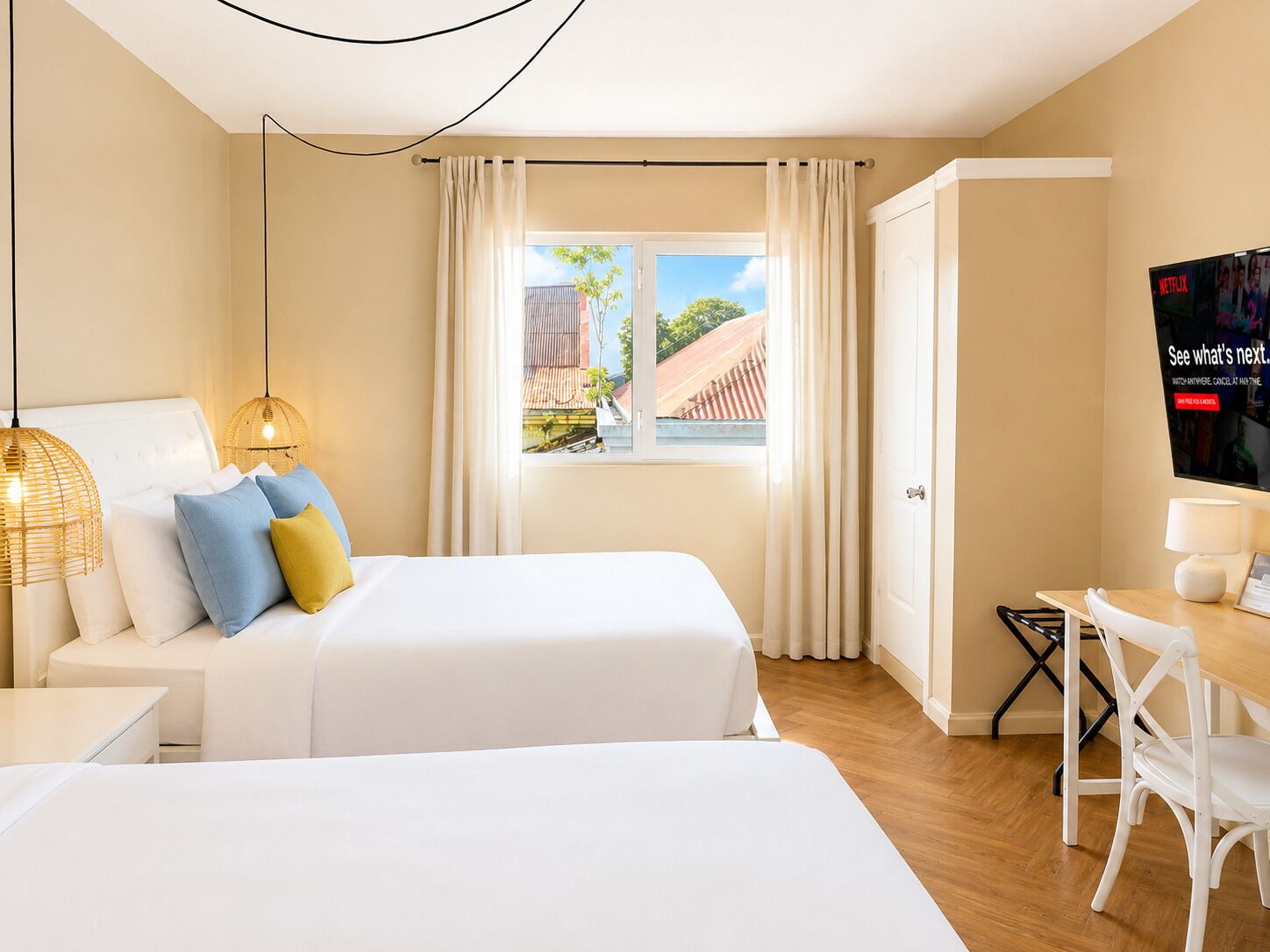 A hotel room with two beds, a TV, a desk, and a window with curtains.