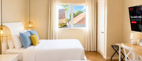 A hotel room with two beds, a TV, a desk, and a window with curtains.