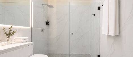 A modern bathroom with a glass-enclosed shower, a white toilet, a vanity with a mirror, and a towel rack.