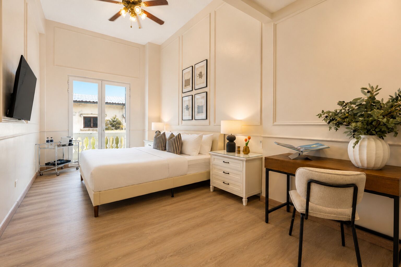 A hotel room with a bed, bedside table, desk, chair, TV, and a view of the outside.
