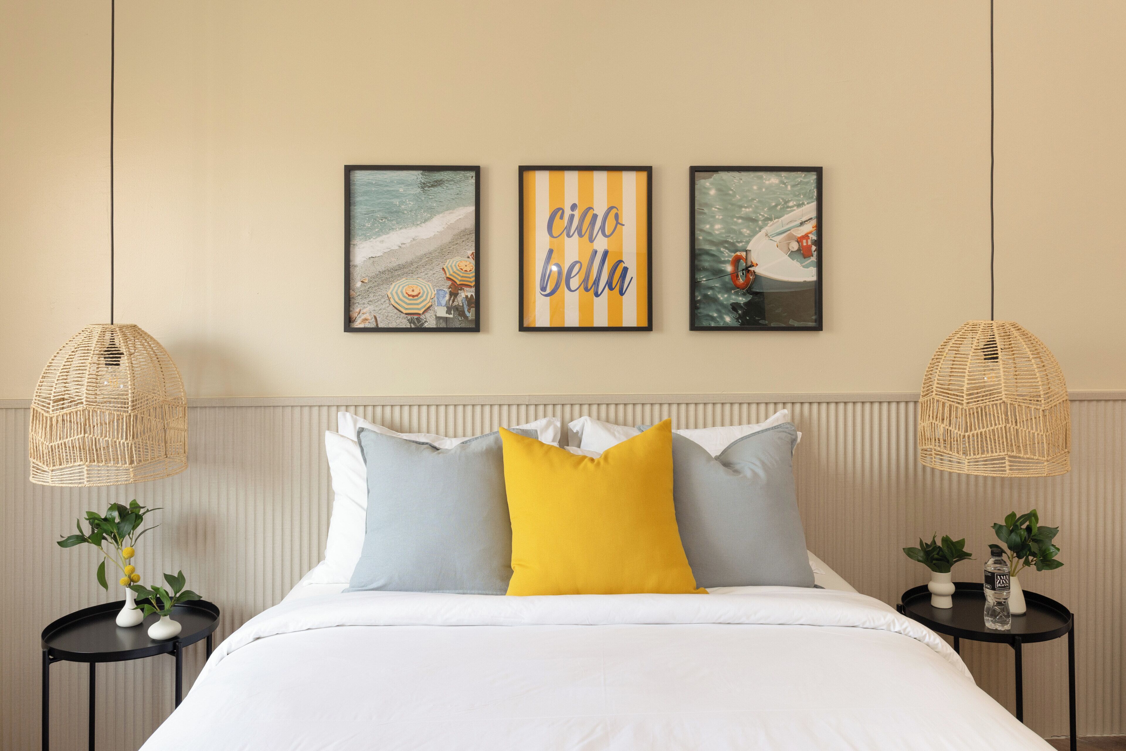 A neatly arranged bedroom with a bed, pillows, a bedside table with a plant, and wall art.