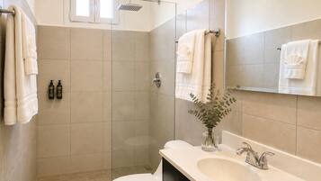 A bathroom with a toilet, sink, mirror, shower, and towels.