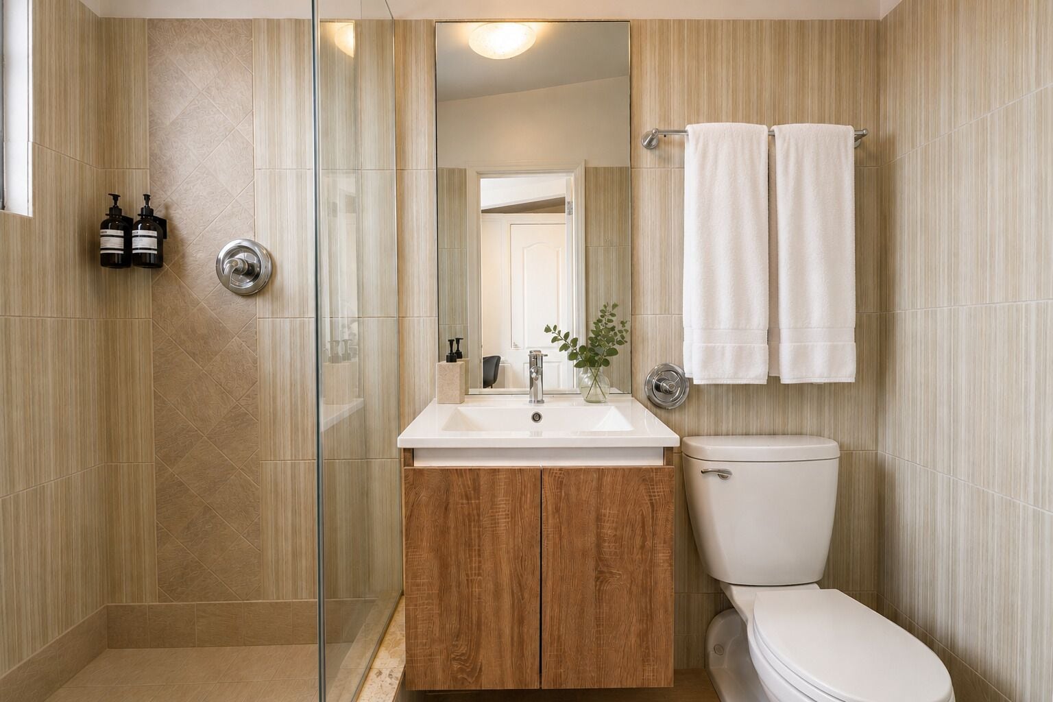 A modern bathroom with a glass shower enclosure, a wooden vanity, a white sink, and a toilet.