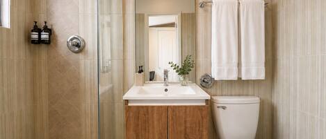 A modern bathroom with a glass shower enclosure, a wooden vanity, a white sink, and a toilet.
