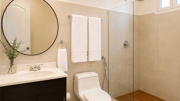 Une salle de bain avec un miroir rond, deux serviettes blanches, des toilettes, une douche et un plancher en bois.