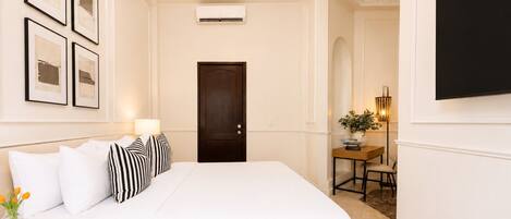 A hotel room with a bed, a desk with a lamp, a TV, and framed pictures on the wall.
