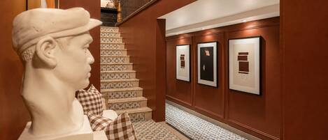 A marble bust, a staircase with patterned tiles, and framed artworks on the wall.