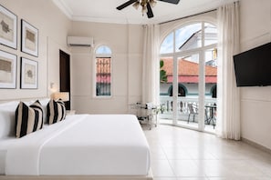 A hotel room with a large bed, a TV, a balcony with a view of the outside, and a window with decorative ironwork. - Magnolia Inn (Panama City)