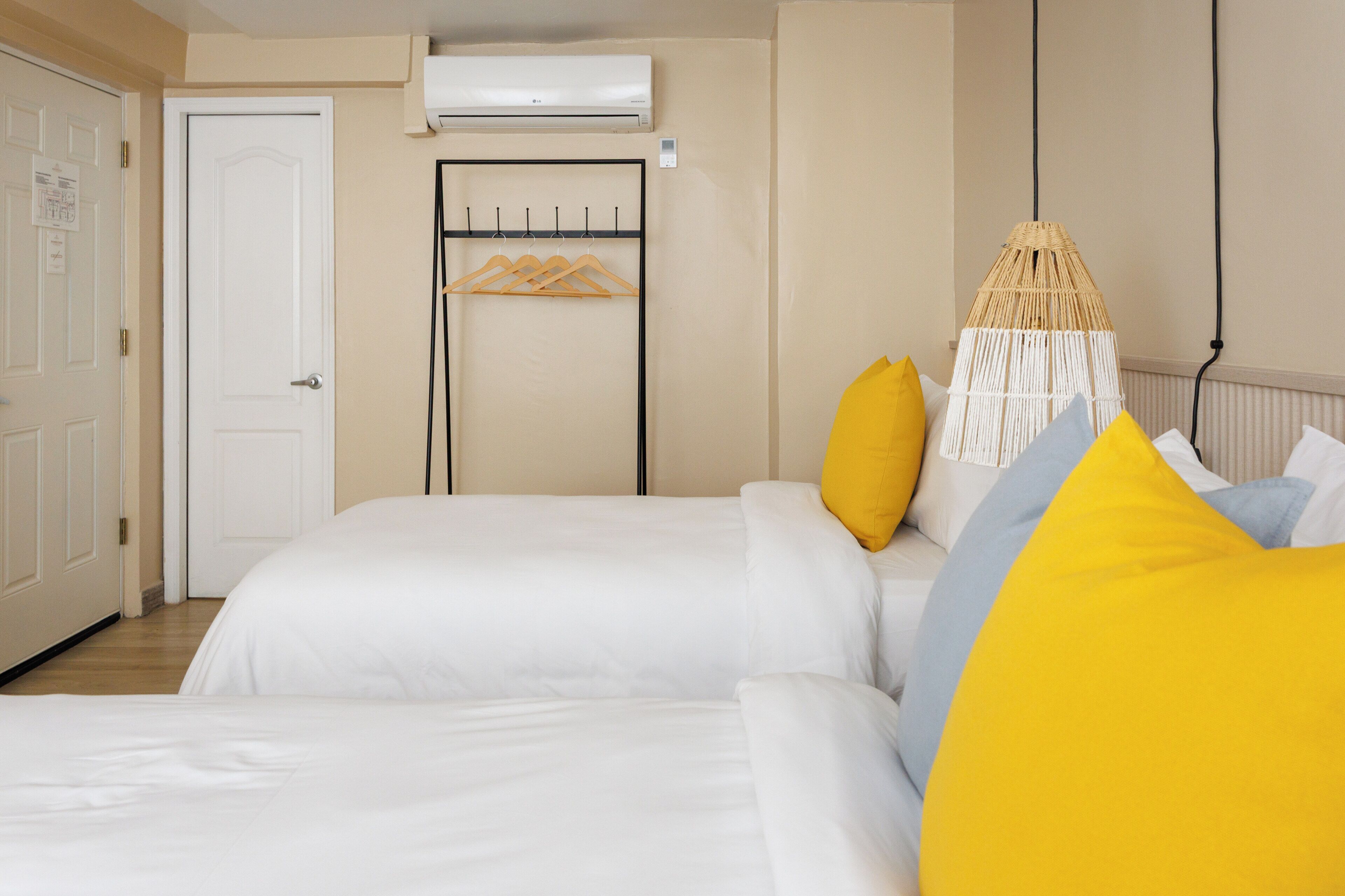A hotel room with two beds, a coat rack, an air conditioning unit, and a hanging lamp.