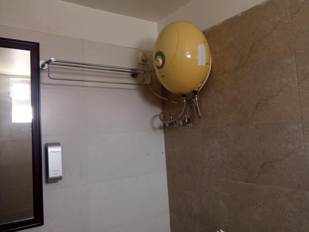 A bathroom with a yellow showerhead mounted on a wall, a towel rack, and a hand dryer.