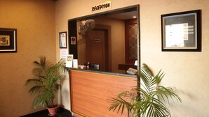 A reception desk with a sign above it, a fan, and framed pictures on the walls. - Hotel Shree Hari Grand (Puri)
