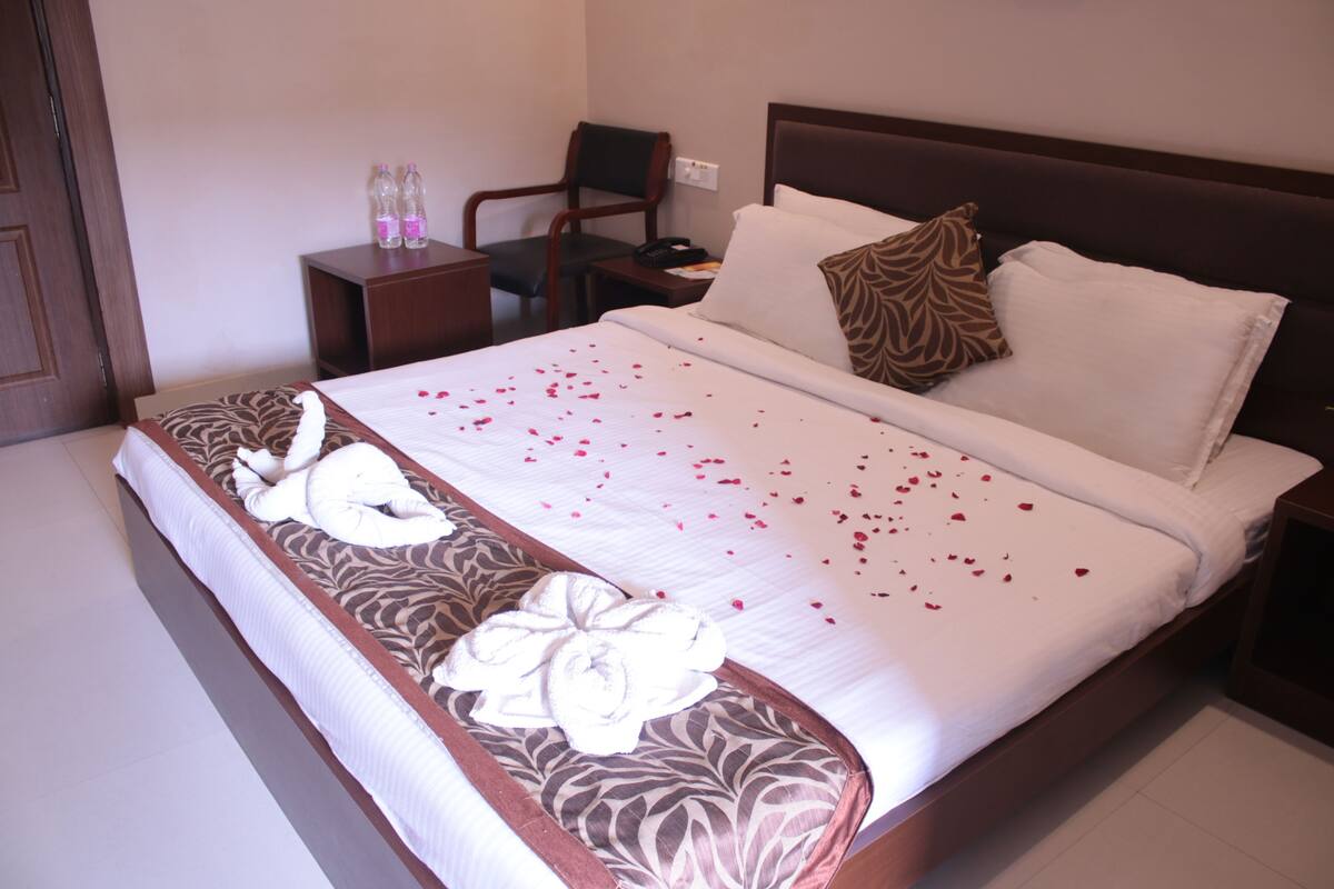 A neatly made bed with rose petals, a pillow, and a decorative towel.