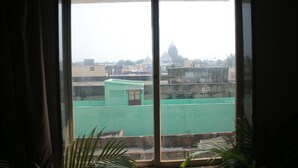 A view through a window with a green fence and a building with a dome in the distance. - Hotel Shree Hari Grand (Puri)