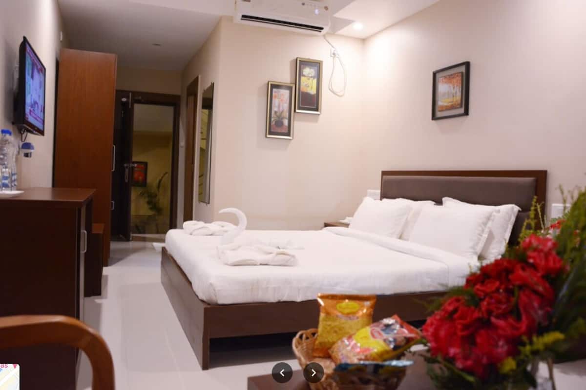 A hotel room with a bed, a desk, a television, and a wall-mounted air conditioner.