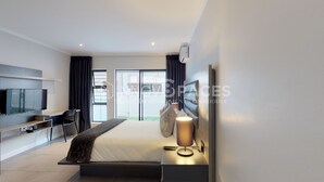 Une chambre moderne avec un lit, une table de chevet, une lampe, un téléviseur et une vue sur l’extérieur.