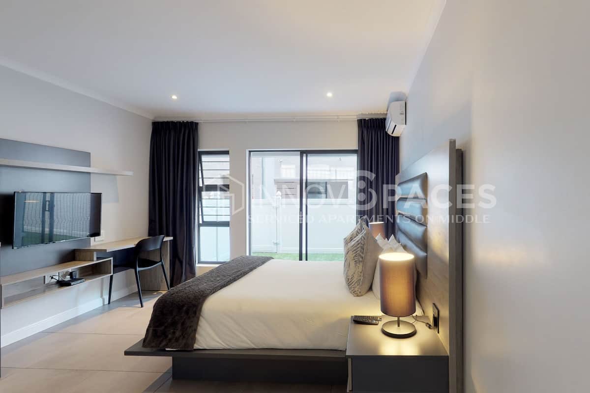 Een moderne slaapkamer met een bed, nachtkastje, lamp, televisie en uitzicht.