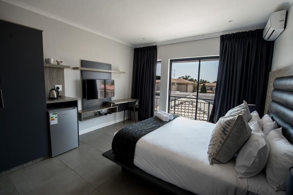A modern hotel room with a bed, a TV, a desk, and a balcony with curtains.