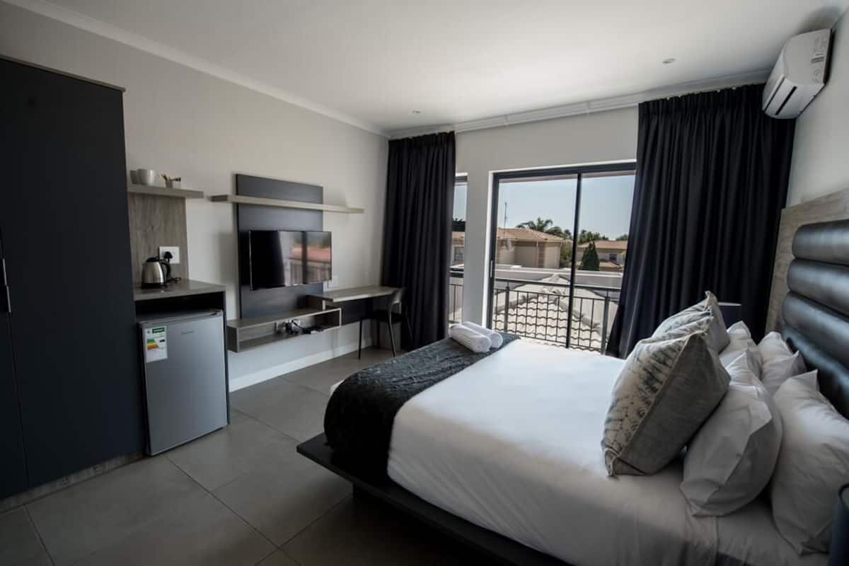 Een moderne hotelkamer met een bed, een televisie, een bureau en een balkon met gordijnen.