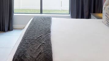 A hotel room with a bed, a window with curtains, and a view of the outside.