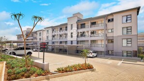 Un immeuble résidentiel à plusieurs étages, doté de balcons, d’un espace de stationnement et d’un panneau indiquant l’emplacement des différents services offerts dans l’immeuble.